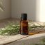 Amber glass bottle of rosemary essential oil with fresh rosemary sprigs on a wooden surface, in natural light